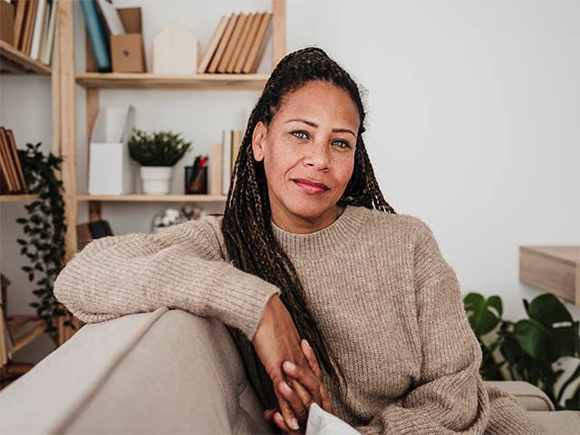 Black woman with long braided hair sits on a couch, resting her arm on the back of it