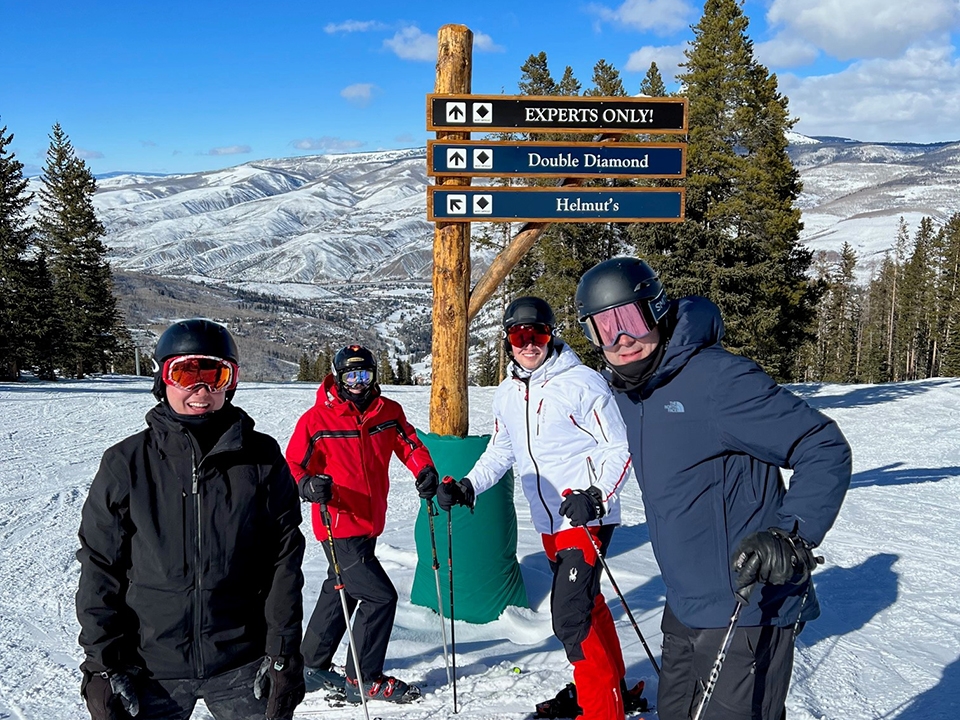 Three people smiling and posing together on a snowy ski slope, surrounded by tall trees.