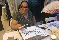 A woman smiles joyfully while holding a sign, celebrating a special occasion in a medical education setting.