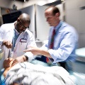 A doctor is examining a patient in an operating room, with residents present to gain practical experience.