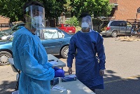 Two individuals in protective gear stand beside a table, promoting CPR training in diverse communities to enhance patient care.