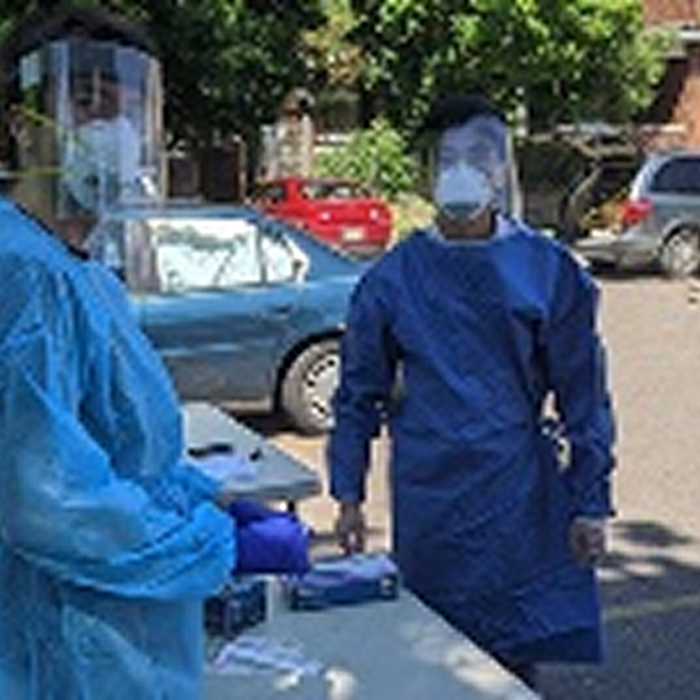 Two individuals in protective gear stand beside a table, promoting CPR training in diverse communities to enhance patient care.