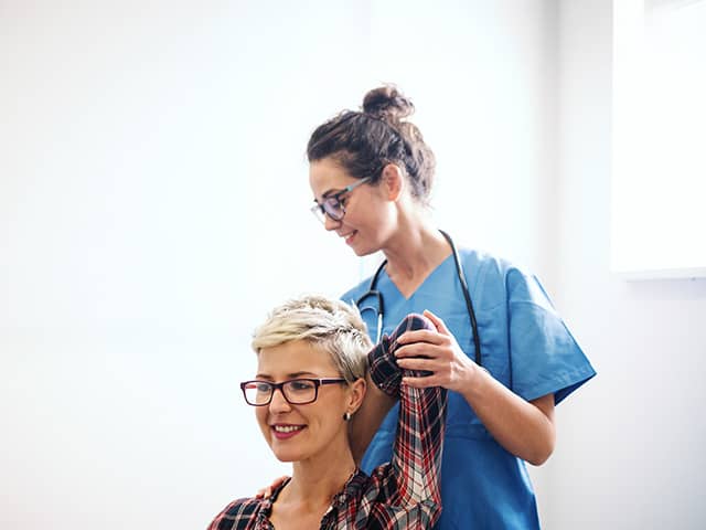 Female medical provider in blue scrubs is checking a female patients arm and shoulder