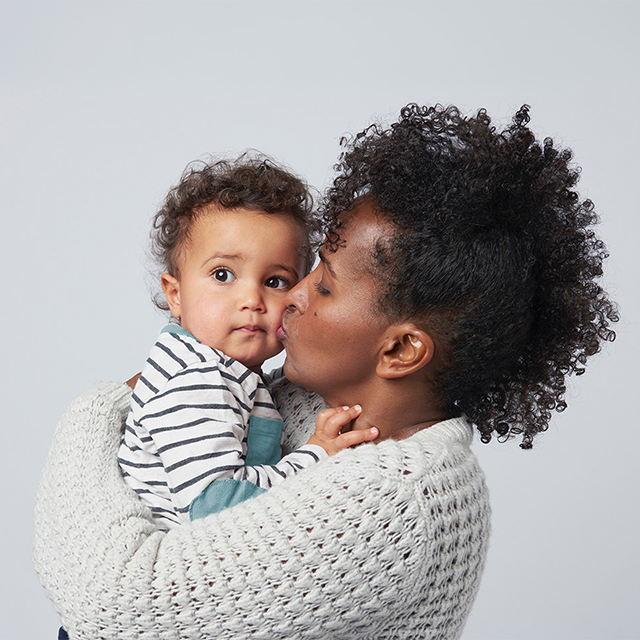 Caregiver holding and kissing an infant child in a studio setting, highlighting comfort, care and infant wellness.