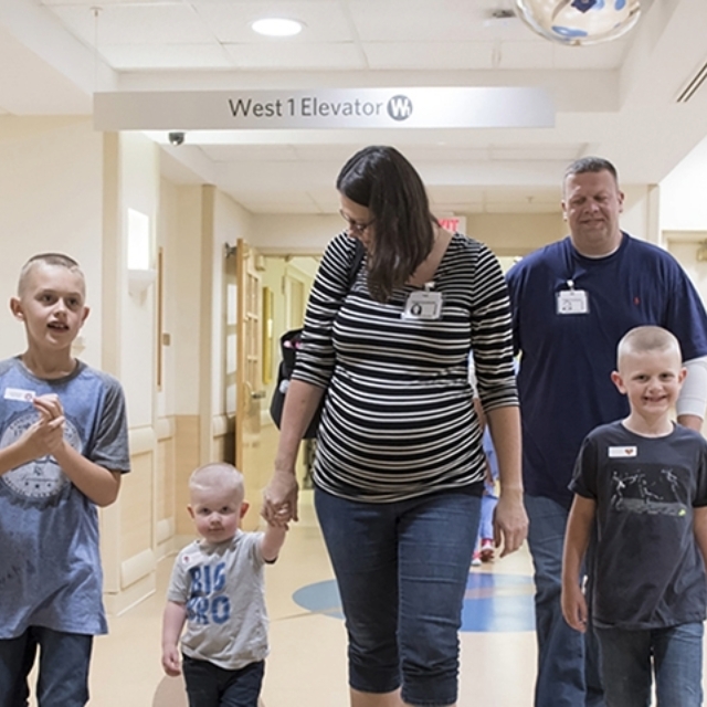 Mother and father with three sons walk into neonatal intensive care unit for a visit