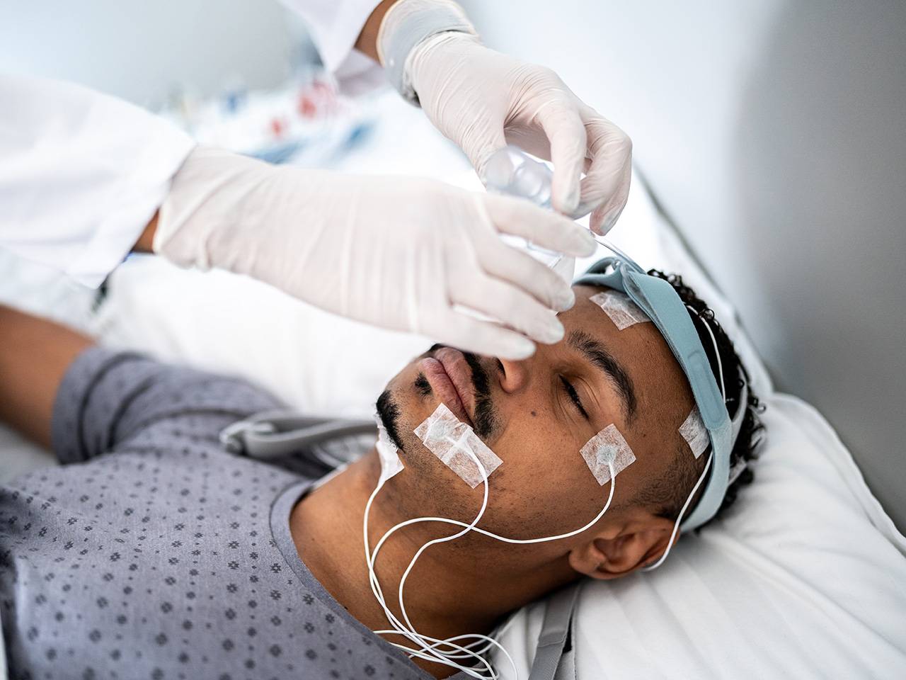 A male patient in the hospital going through a sleep study is getting sensors placed on his head and face