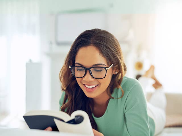 Smiling young woman with brown hair and glasses reads a book