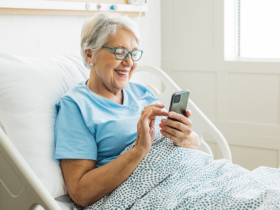 Hospital patient using a smartphone in a hospital bed to access health information and manage care during a stay.