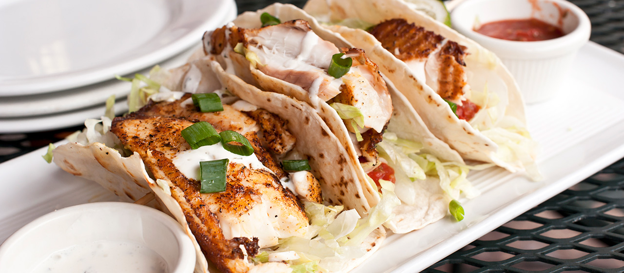 Plate of fish tacos topped with lettuce and green onions, served with sauce as a fresh, flavorful meal.