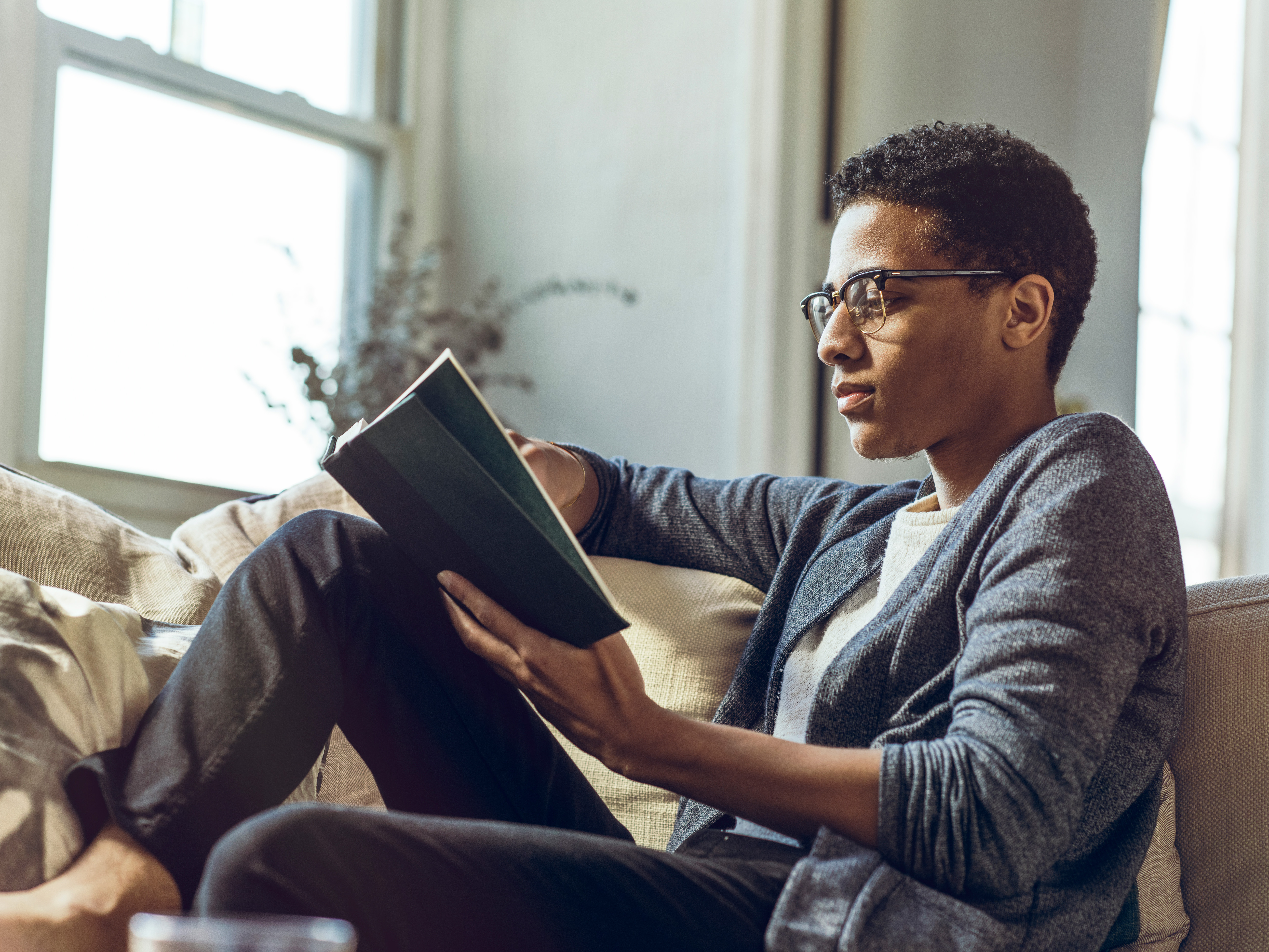 A man wearing glasses is focused on reading a book.