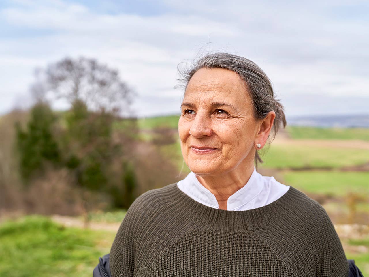 White woman with hair pulled back into a bun stands in a field outdoors
