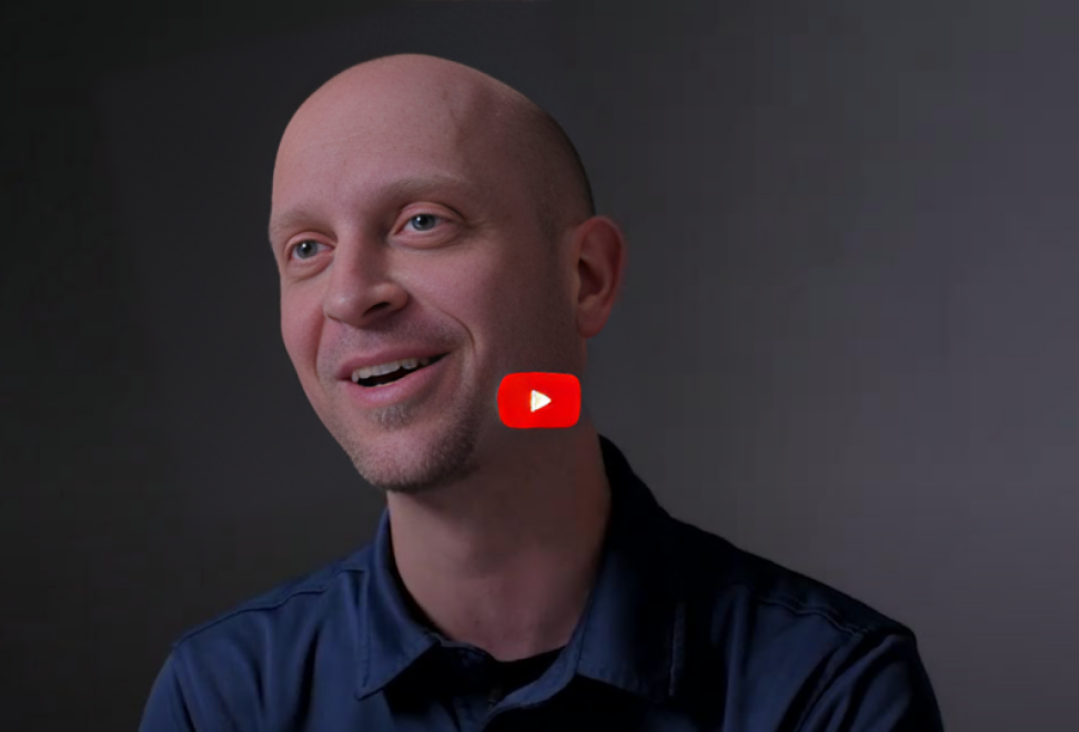 Man in dark blue shirt sitting in front of dark backdrop