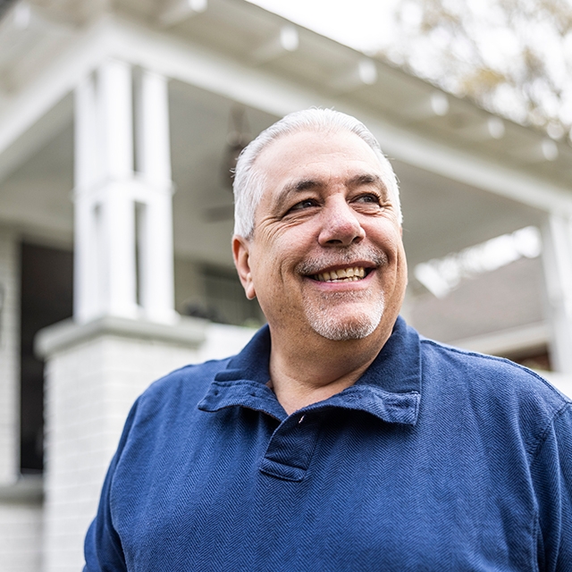 A smiling man stands in front of a house.