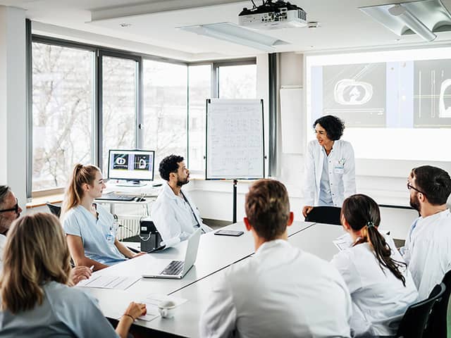 Group of medical professionals in white coats sitting around a table talking