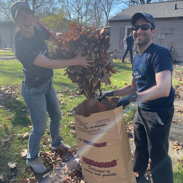 Two medical students smiling while raking and filling paper leaf bags up 