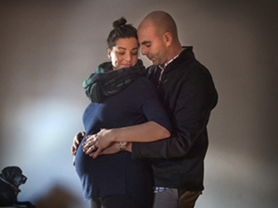 Man hugs his pregnant partner from behind with hands on her belly