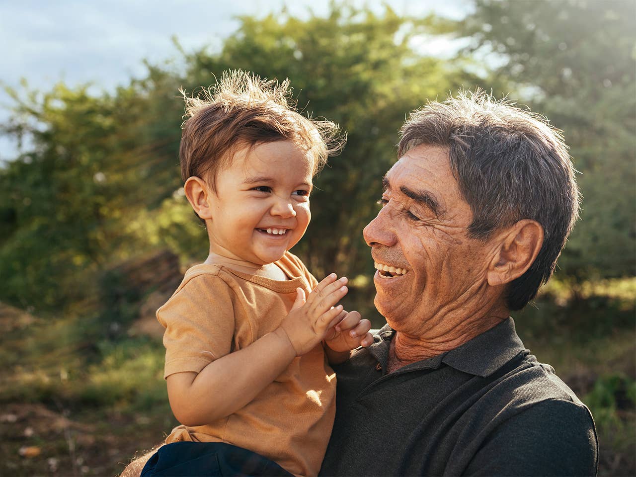 Older man holding a young boy while outside smiling 