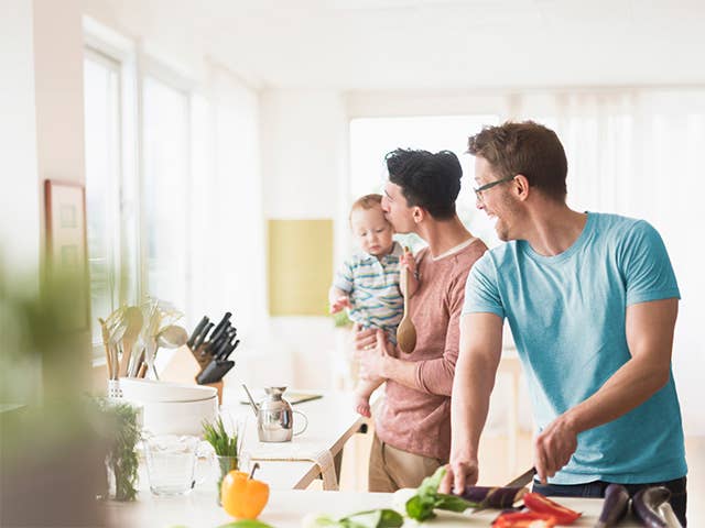 Two men cooking in kitchen, as one holds a toddler