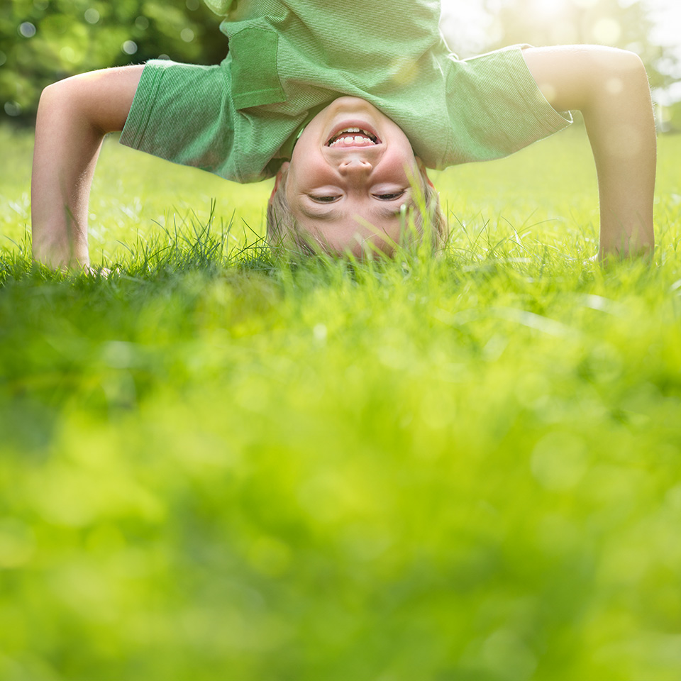 Young boy with blond hair and green t-shirt does a headstand in the grass