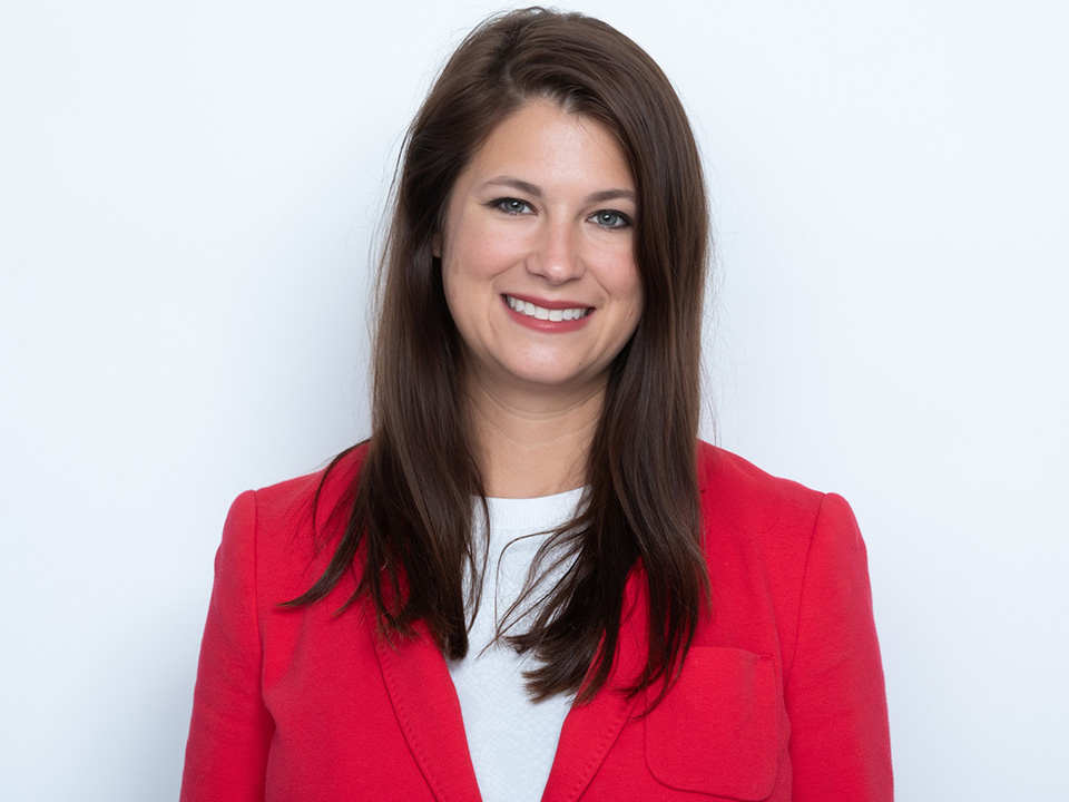 Natalie Baggio, RN, woman with long brown hair wearing a red sportcoat with a white shirt