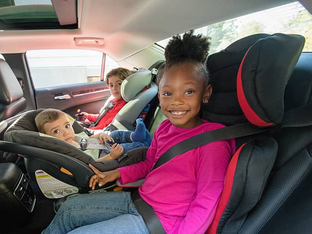 Three children sitting in car seats in the back seat of a vehicle