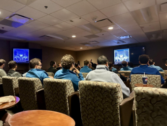A diverse group of people in chairs, attentively listening to a speaker in a conference room setting.