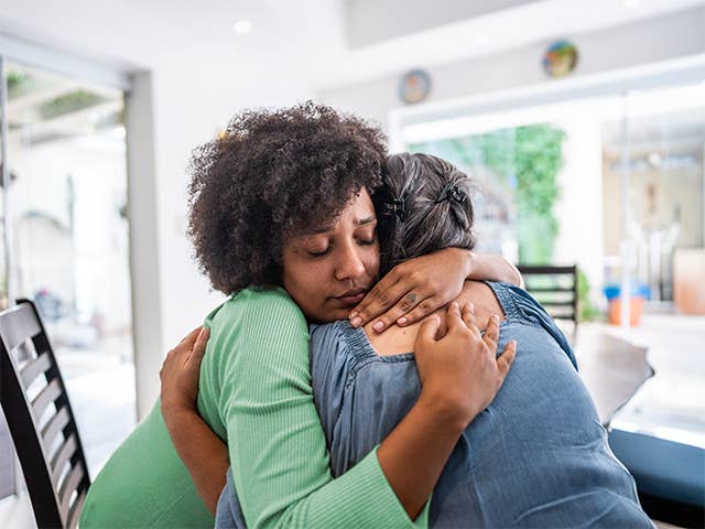 Young Black woman wearing a green shirt gets a hug from an older Black woman