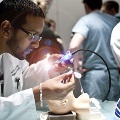 A man in a lab coat conducts an experiment on a medical dummy, surrounded by residents observing the process.