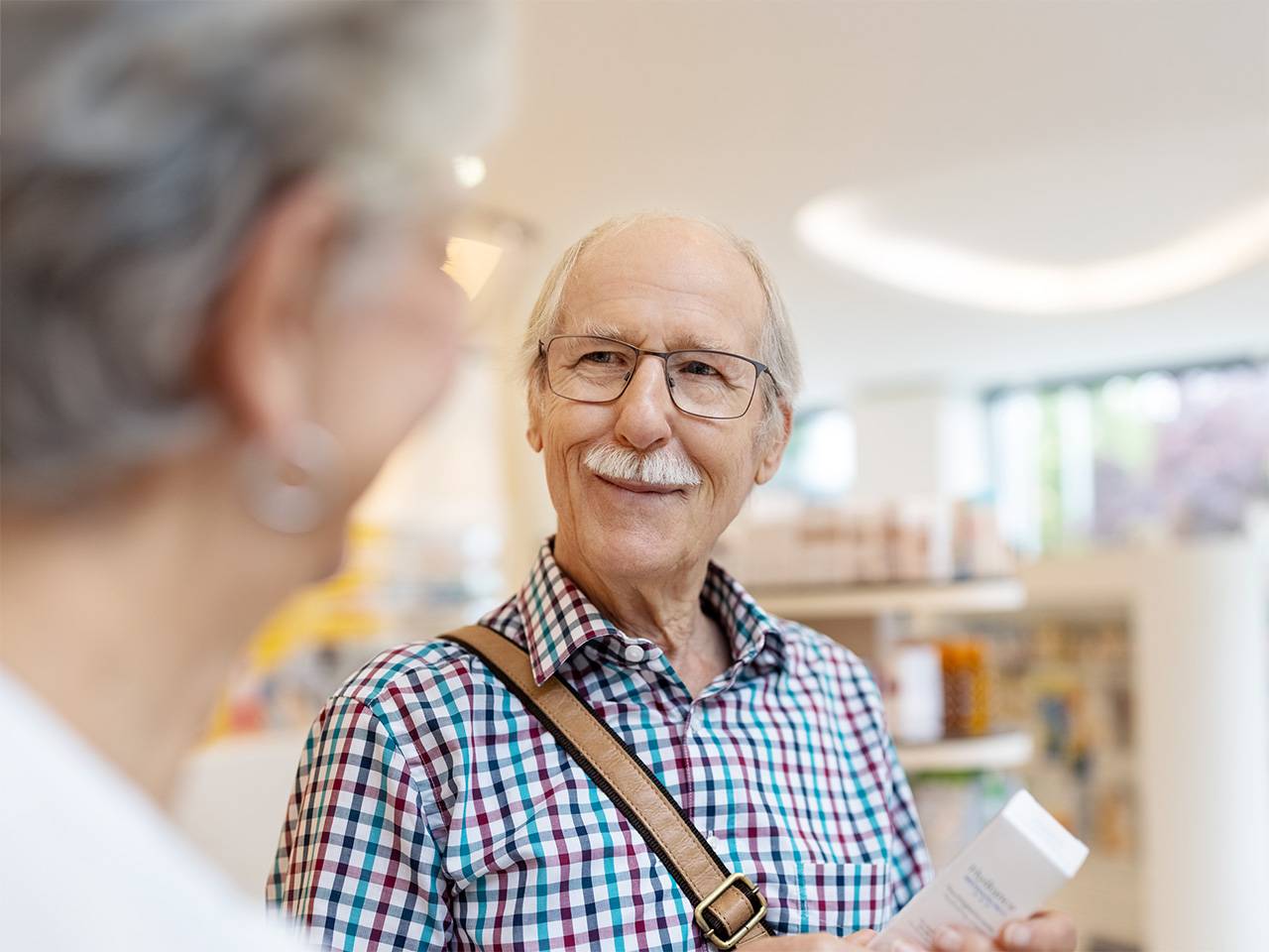 Older white man with white hair and moustache smiles and speaks with a Corewell Health pharmacy team member
