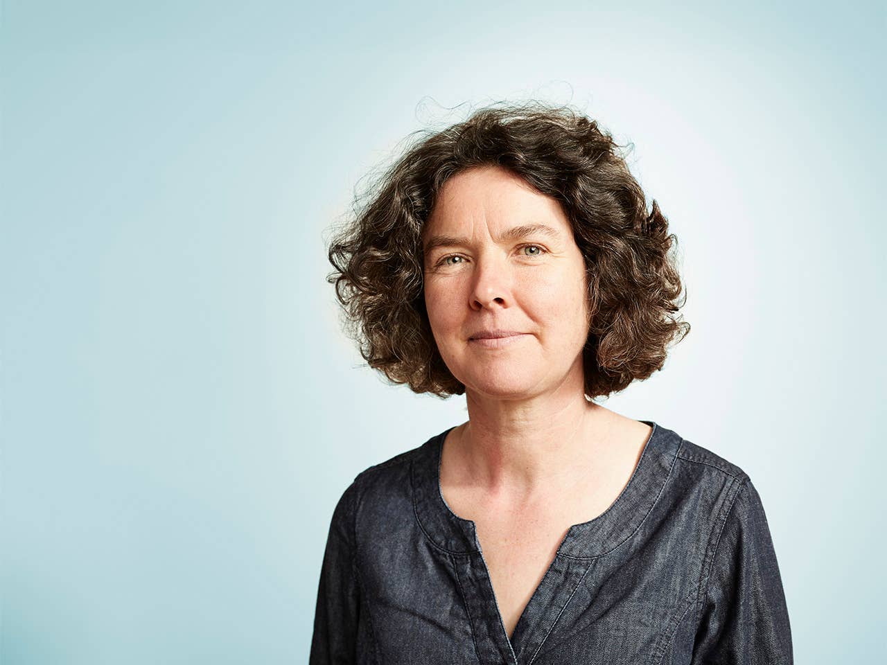 Middle aged white woman with brown hair standing in front of a light blue background