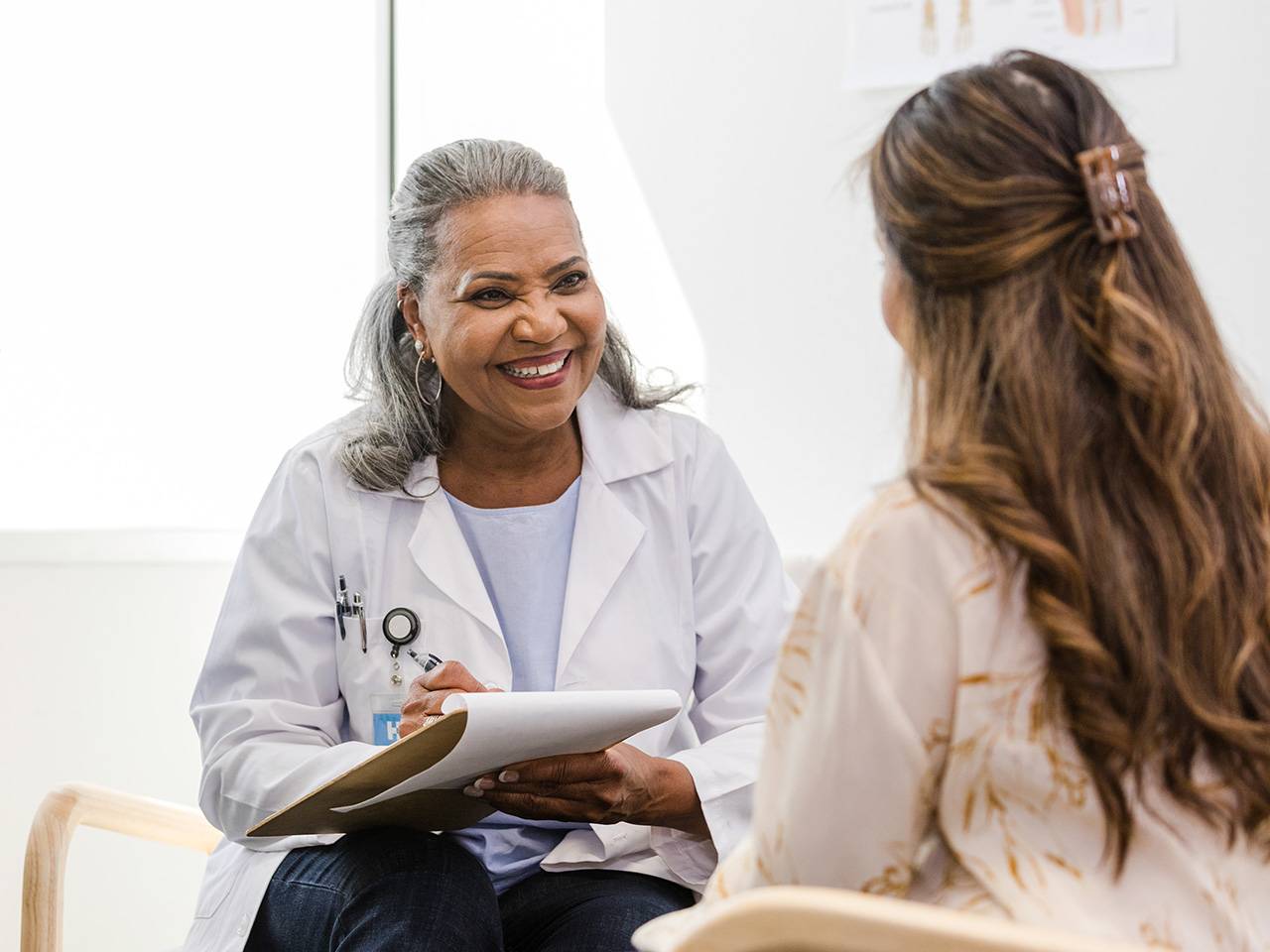 A smiling Corewell Health employer services team member sits across from a female patient as she takes notes on a clipboard