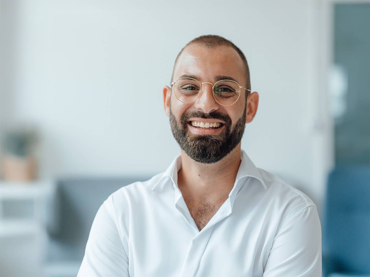 Smiling young white man with glasses and a beard inside a white room