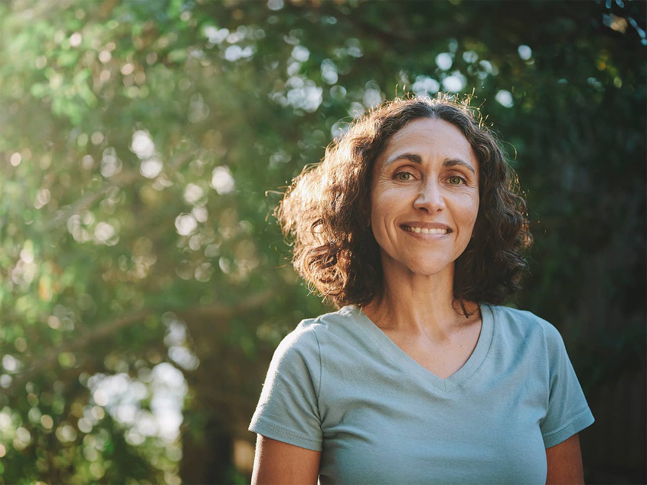 Smiling woman in a light blue shirt with shoulder length curly brown hair