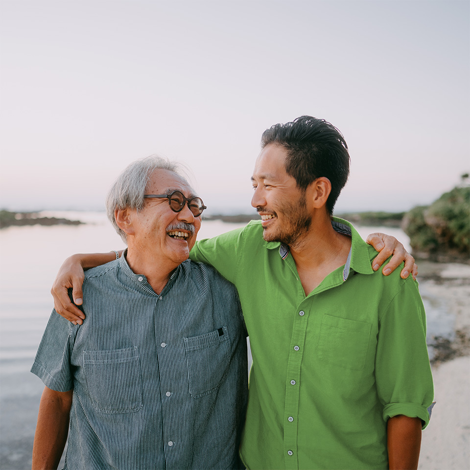 Older Asian man looks at son as they smile and hug