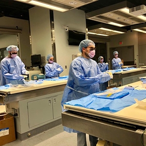 Several professionals in blue scrubs work together at a table, focusing on case-based learning in an emergency medicine setting.