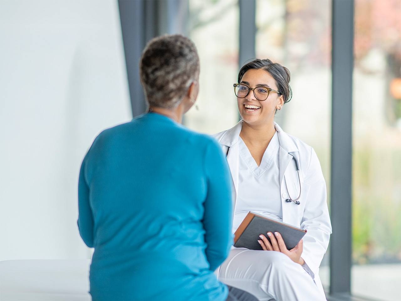 A female doctor is smiling and having a conversation with her female patient with holding a tablet