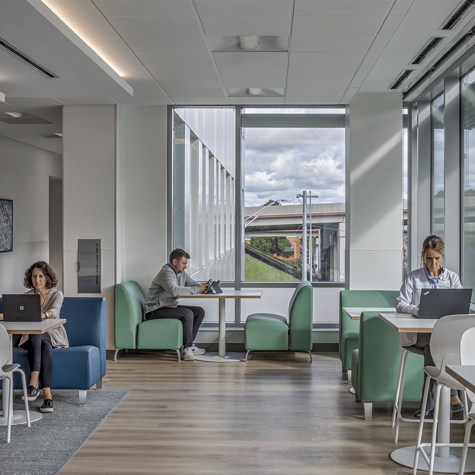 People are seated at tables in a spacious open office area, engaged in work and discussions.