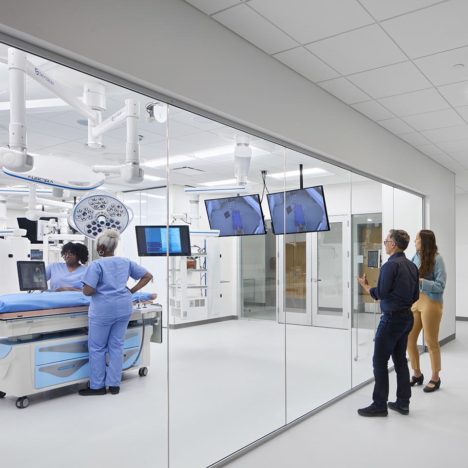 A group of health care professionals gathered in a room, viewing a monitor.
