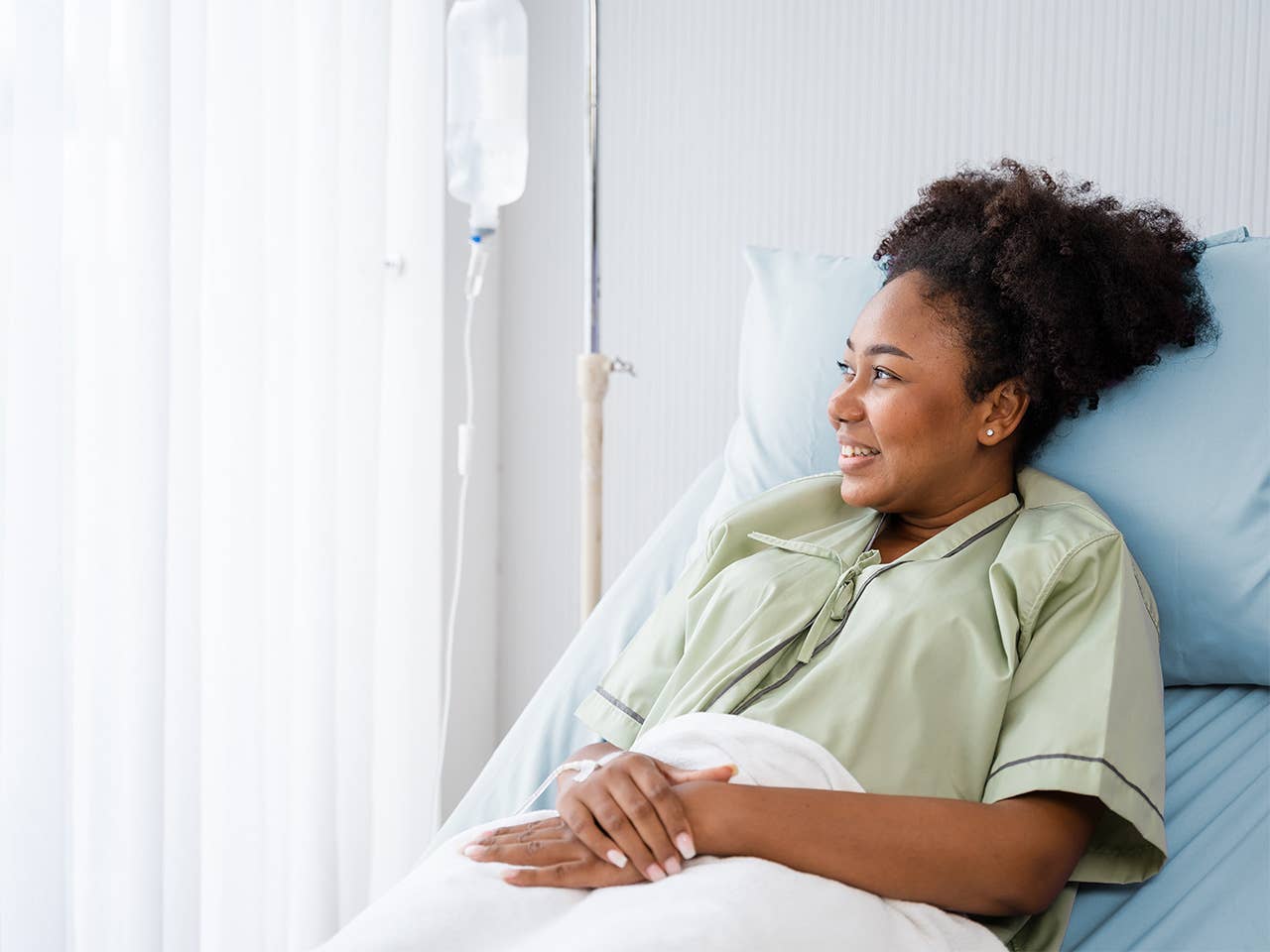Black woman with curly hair rests in a hospital bed