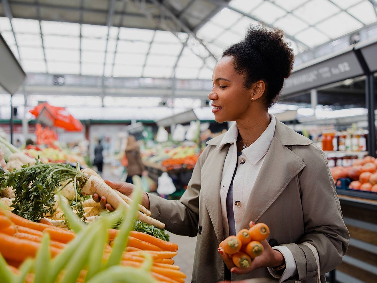 Person selecting fresh carrots and root vegetables at a market, finding healthy foods that fit a budget.