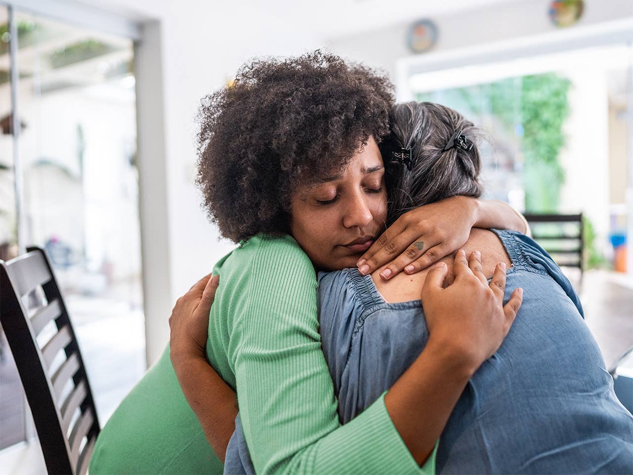 Young Black woman wearing a green shirt gets a hug from an older Black woman