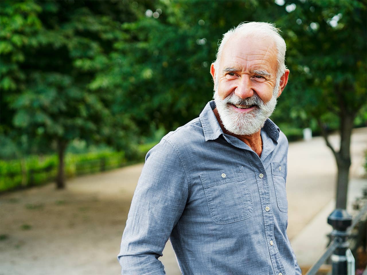 Smiling older man with white hair and white beard standing in a forest