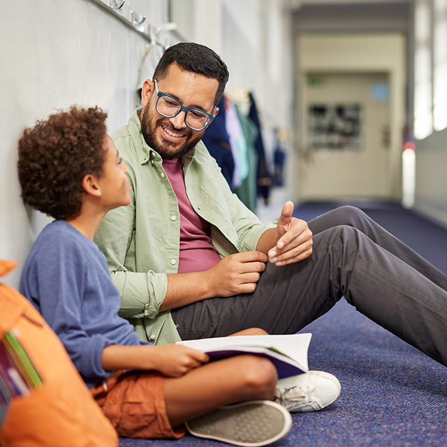 A man and a boy sit together on the floor, engaged in a conversation or activity.