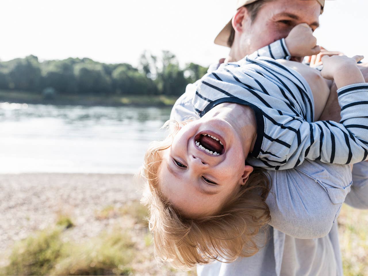 Smiling boy is being held over his smiling fathers should while outside by the lake.