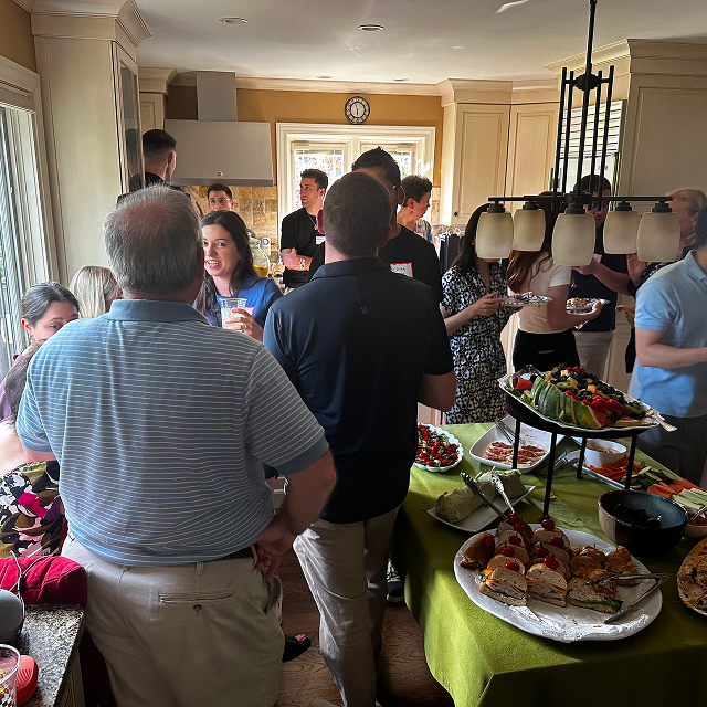 Attendees mingle around a buffet table at an indoor reception, with food platters and refreshments on display.