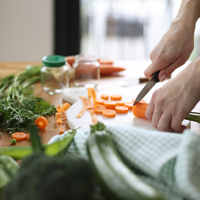 A person chopping colorful vegetables on a wooden table in a well-lit kitchen.