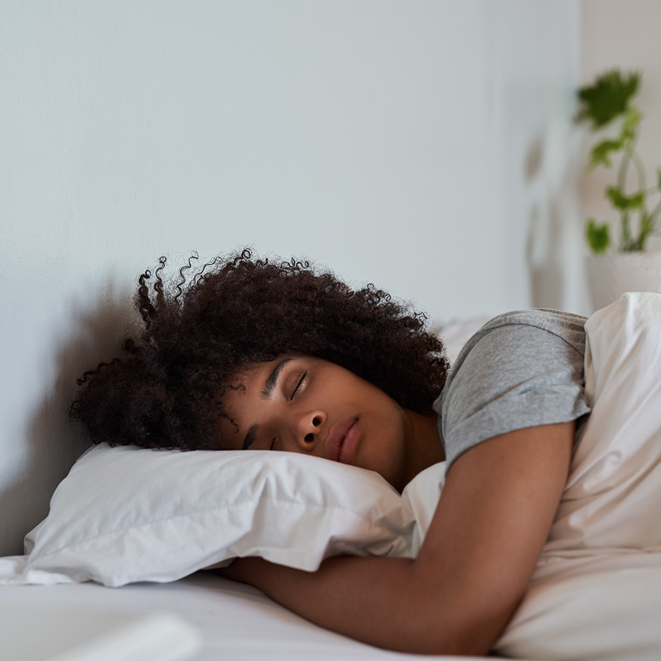 Black woman with curly brown hair lies down in bed with a pillow
