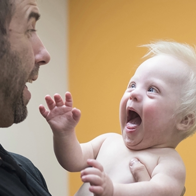 Smiling man lifts a smiling baby boy in the neurodevelopmental pediatrics clinic