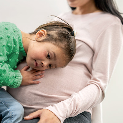 Young girl in a green shirt lays her head on her pregnant mother's stomach