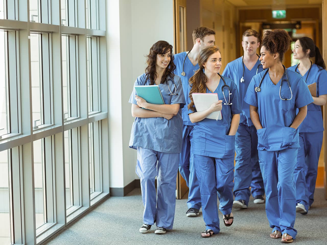 A group of medical students in scrubs walking in a hallway, engaged in conversation.